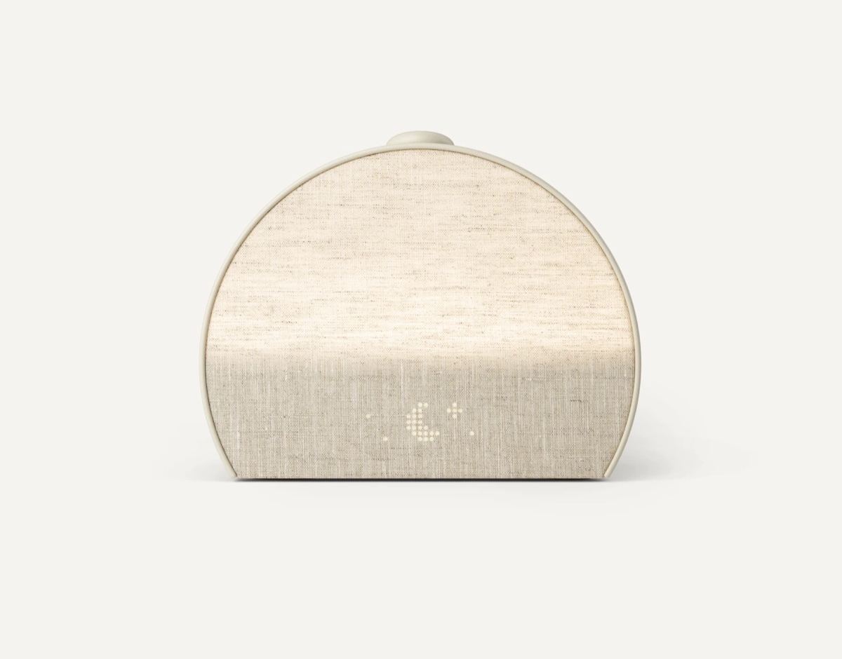 Hatch Restore 3 sunrise alarm clock in putty color with curved fabric body and soft glowing light on a nightstand