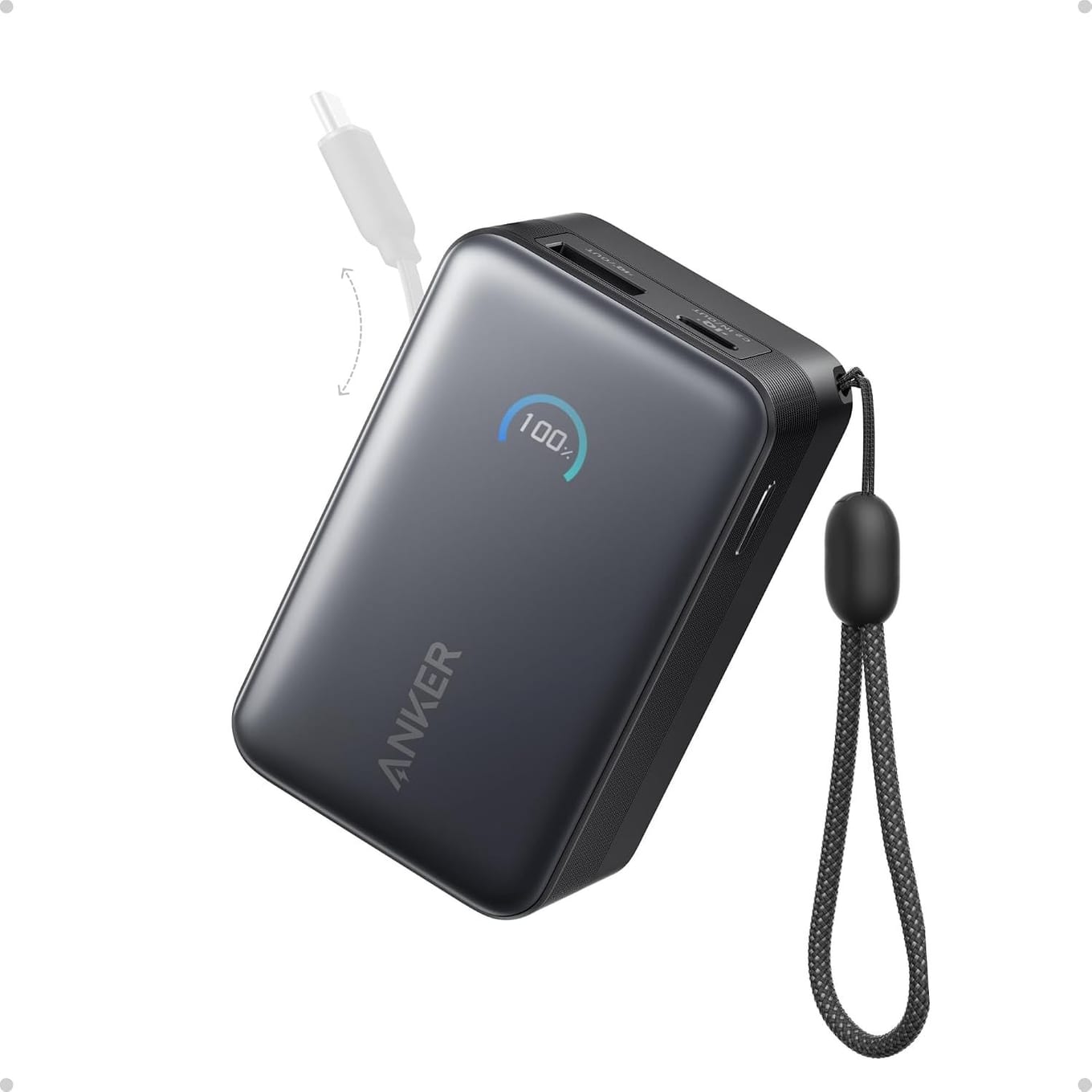 Dark grey Anker power bank at an angle, its round display reading 100%, a USB-A and a USB-C port on its top edge, a braided wrist strap at its side and a faded image of its USB-C cable pulled out of the top