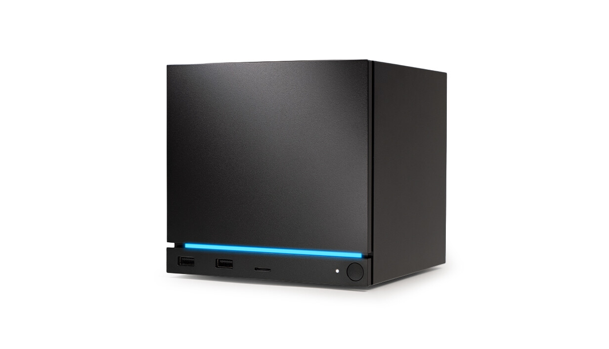 Black Valve Steam Machine cube seen at an angle against white, a blue light strip running above its two front USB ports, microSD slot and power button