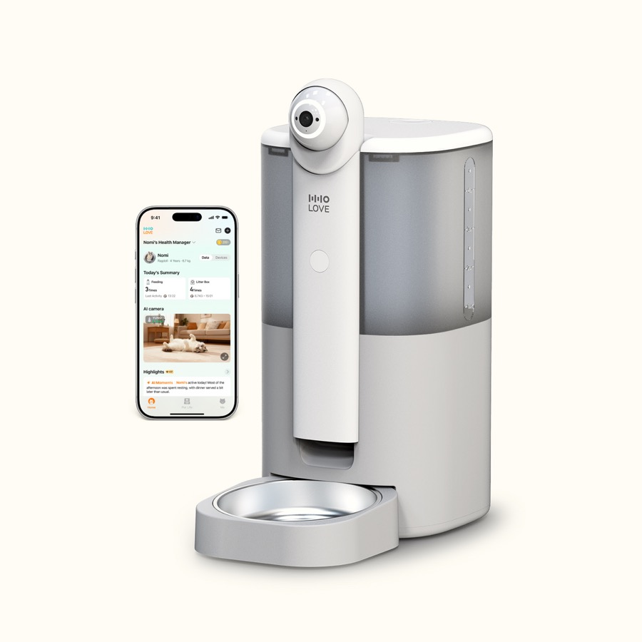 HHOLOVE Yuno white automatic pet feeder with rotating 2K camera head and stainless bowl beside a phone showing the pet monitoring app